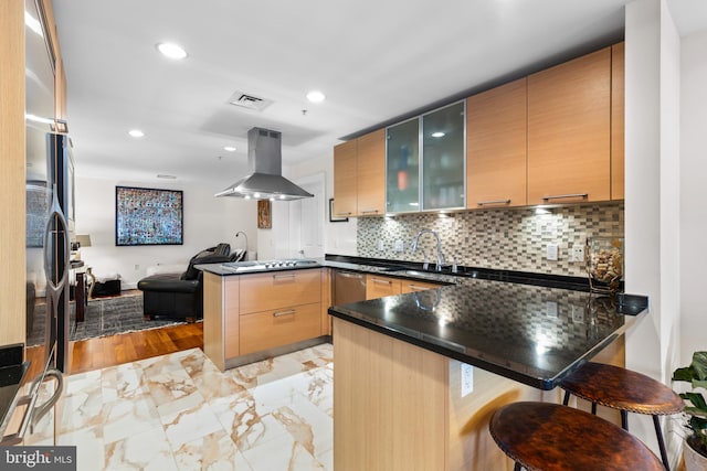 kitchen featuring glass insert cabinets, open floor plan, a sink, island range hood, and a peninsula