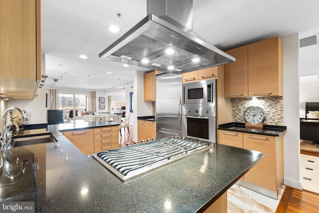 kitchen with built in appliances, island range hood, a peninsula, a sink, and decorative backsplash