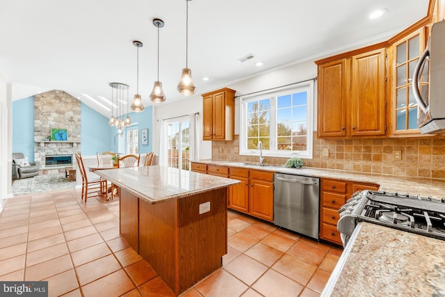 kitchen featuring a sink, a kitchen island, stainless steel appliances, a stone fireplace, and lofted ceiling