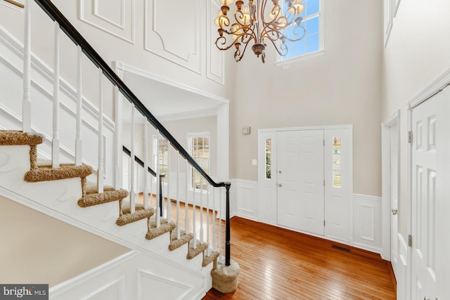 foyer entrance featuring visible vents, a towering ceiling, a wainscoted wall, and hardwood / wood-style flooring