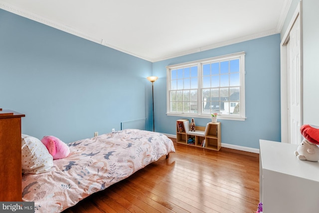 bedroom with baseboards, wood-type flooring, a closet, and crown molding