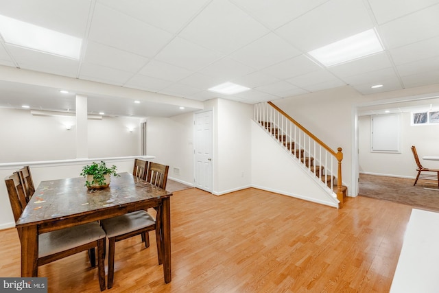 dining space featuring a drop ceiling, stairway, baseboards, and light wood-style flooring