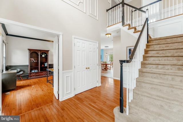 foyer featuring a wainscoted wall, ornamental molding, hardwood / wood-style floors, stairway, and a high ceiling