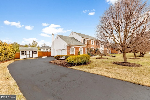 view of property exterior with an outbuilding, fence, a yard, a garage, and aphalt driveway