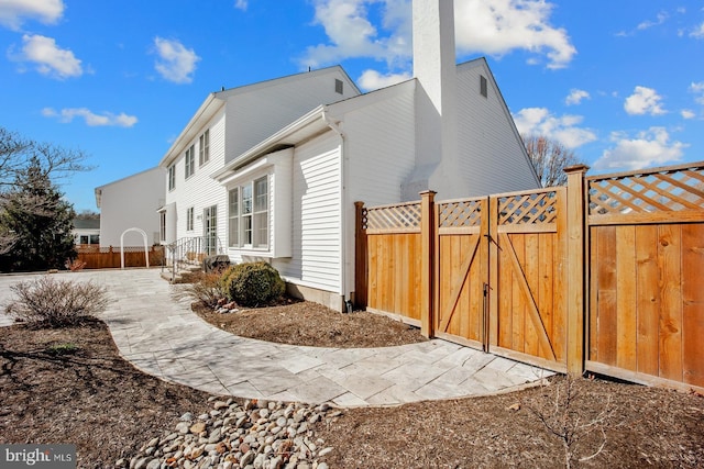 view of side of property with a chimney, fence, and a gate