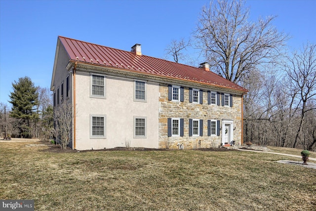 exterior space with metal roof, stone siding, a front lawn, a standing seam roof, and a chimney