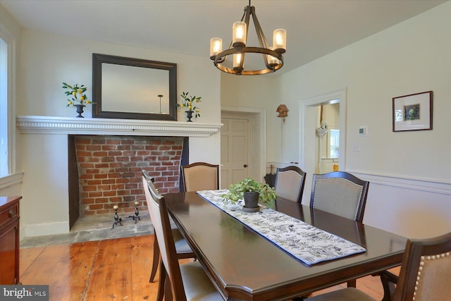 dining room with a chandelier, a brick fireplace, baseboards, and light wood finished floors