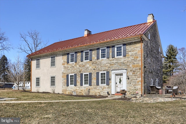 colonial inspired home with a standing seam roof, metal roof, a chimney, and a front lawn