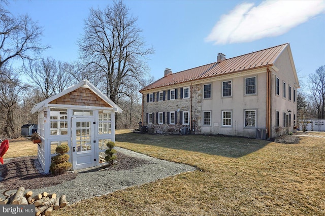 rear view of property with an outbuilding, a chimney, a lawn, a standing seam roof, and metal roof