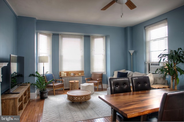 living area with cooling unit, wood finished floors, a ceiling fan, baseboards, and radiator