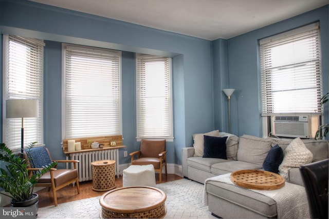 living area with radiator, baseboards, cooling unit, and wood finished floors