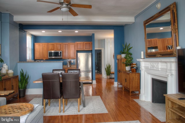 kitchen featuring stainless steel appliances, a ceiling fan, baseboards, light wood-style floors, and beamed ceiling