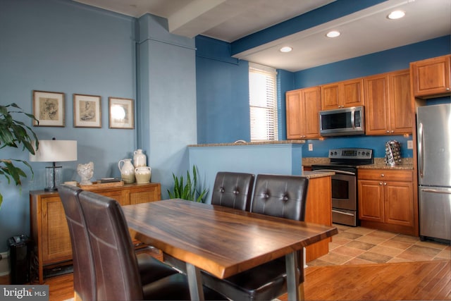 kitchen with appliances with stainless steel finishes, brown cabinetry, beam ceiling, and recessed lighting