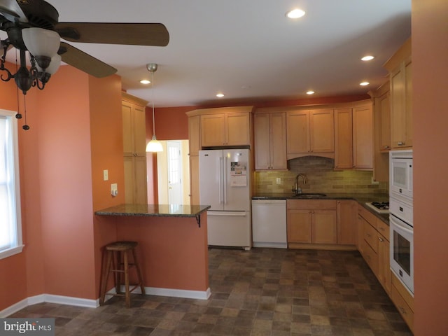 kitchen with a peninsula, white appliances, a sink, backsplash, and decorative light fixtures