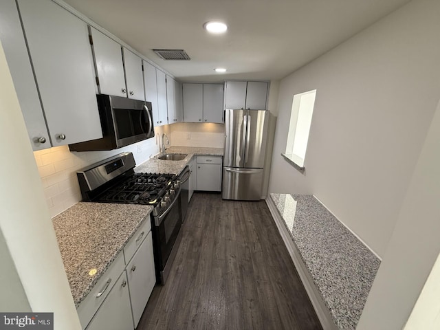 kitchen featuring stainless steel appliances, a sink, visible vents, decorative backsplash, and dark wood-style floors