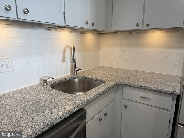 kitchen featuring dishwashing machine, backsplash, a sink, and light stone countertops