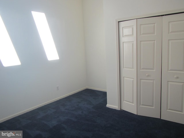 unfurnished bedroom with a closet, dark carpet, and baseboards