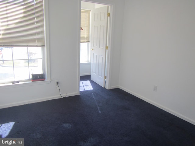 unfurnished room with dark colored carpet, plenty of natural light, and baseboards