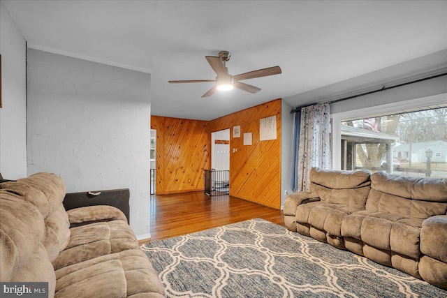 living area with wood walls, wood finished floors, a ceiling fan, and crown molding