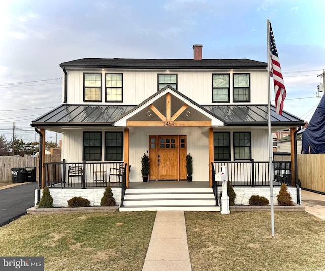 modern farmhouse style home featuring a standing seam roof, fence, covered porch, and a chimney