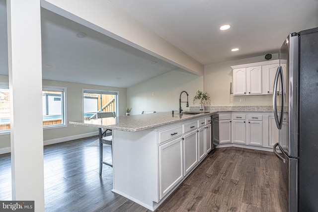 kitchen featuring dark wood-style floors, a peninsula, freestanding refrigerator, a sink, and white cabinets