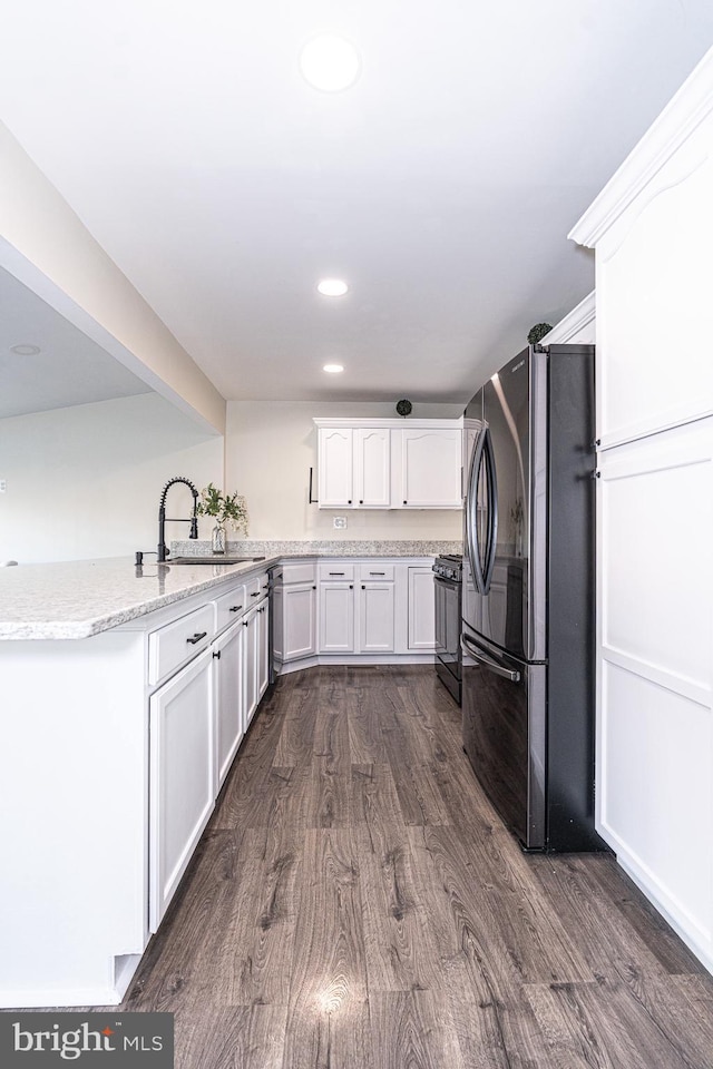 kitchen featuring gas stove, a peninsula, freestanding refrigerator, a sink, and dark wood-type flooring