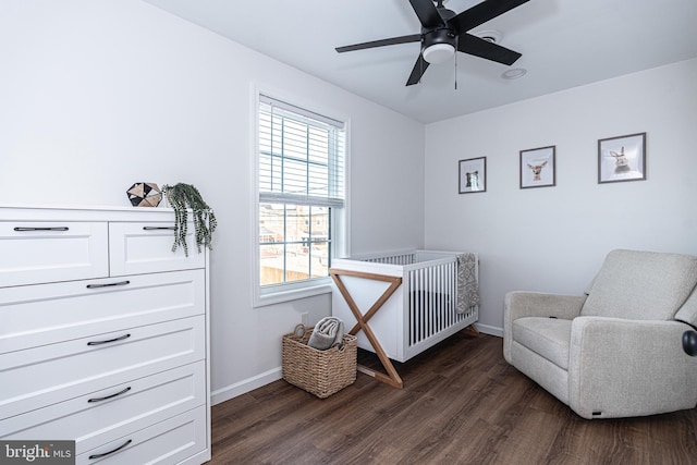 bedroom with baseboards, a nursery area, dark wood-style floors, and a ceiling fan