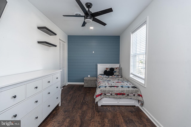 bedroom featuring dark wood finished floors, baseboards, wood walls, and ceiling fan