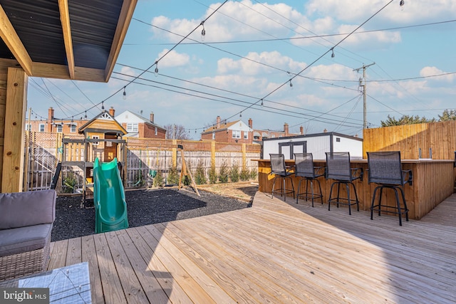 wooden terrace with a playground, a fenced backyard, and outdoor dry bar