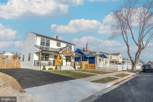 view of front of house with a standing seam roof, a fenced front yard, a porch, a residential view, and metal roof