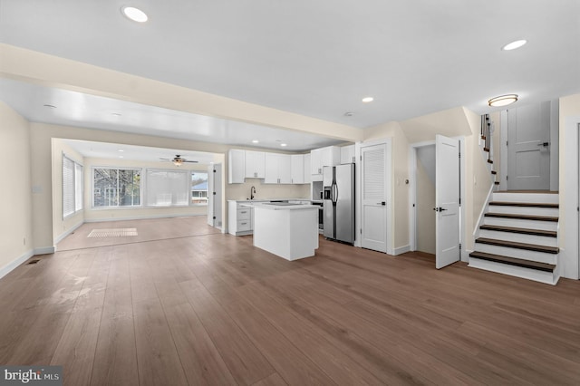 kitchen with light countertops, white cabinetry, wood finished floors, stainless steel fridge, and open floor plan