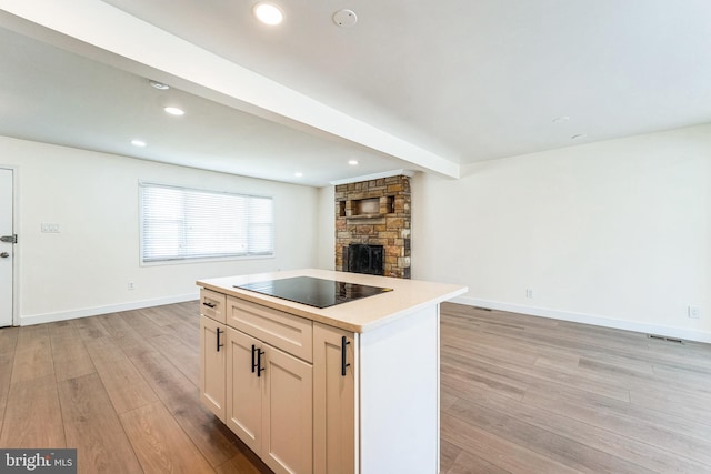 kitchen featuring a stone fireplace, black electric cooktop, light wood-type flooring, and open floor plan