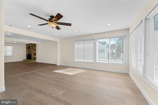 unfurnished living room with a fireplace, ceiling fan, light wood finished floors, and a wealth of natural light