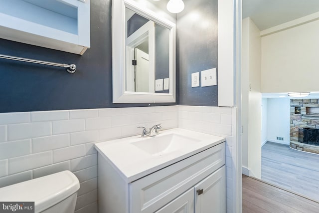 half bath featuring tile walls, toilet, vanity, and a stone fireplace