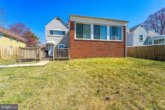 rear view of house featuring a wooden deck, fence, brick siding, and a yard