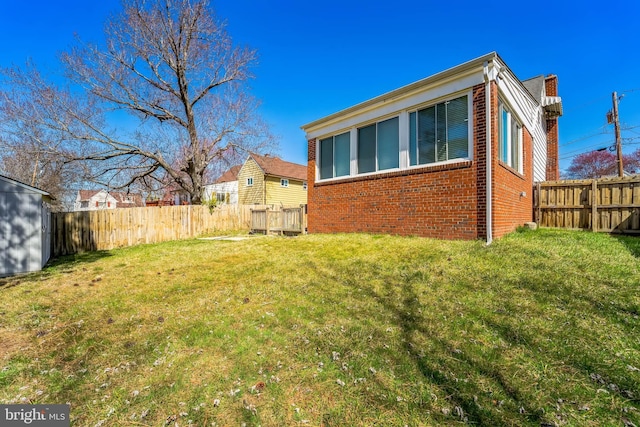 view of side of property featuring brick siding, an outbuilding, a fenced backyard, and a yard