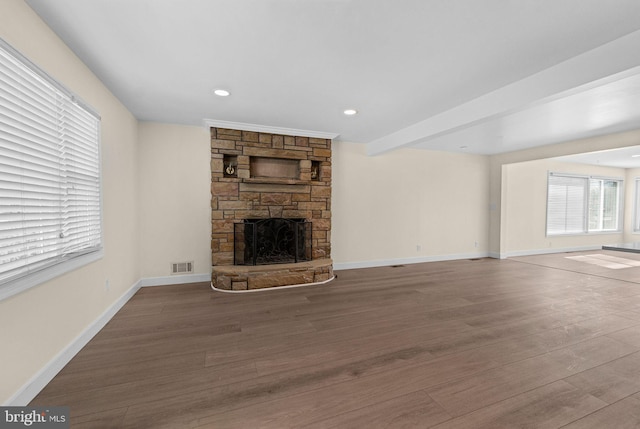 unfurnished living room with baseboards, visible vents, wood finished floors, and a stone fireplace