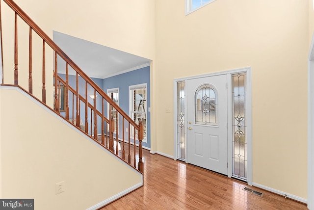 foyer entrance with baseboards, visible vents, wood finished floors, stairs, and crown molding