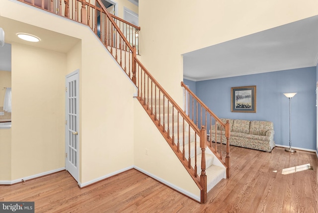 stairway with ornamental molding, wood finished floors, a towering ceiling, and baseboards