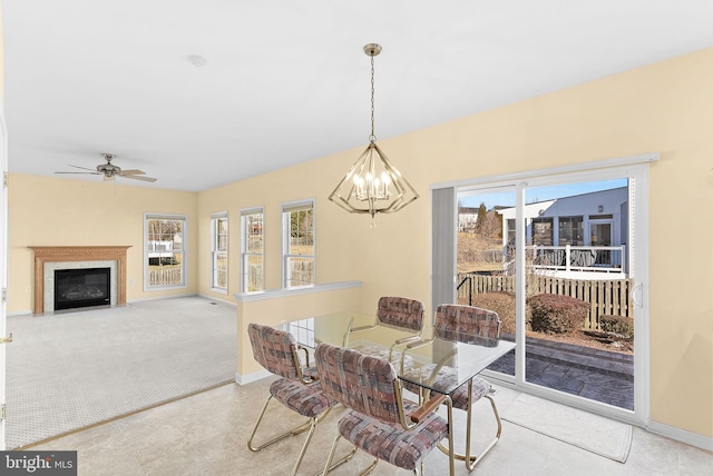 dining space with ceiling fan with notable chandelier, carpet floors, a fireplace with flush hearth, and baseboards