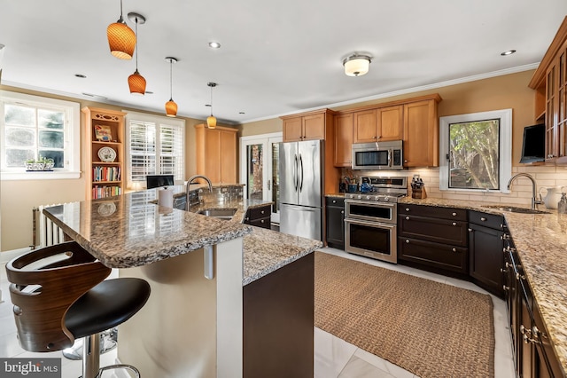 kitchen with crown molding, decorative backsplash, appliances with stainless steel finishes, a kitchen breakfast bar, and a sink