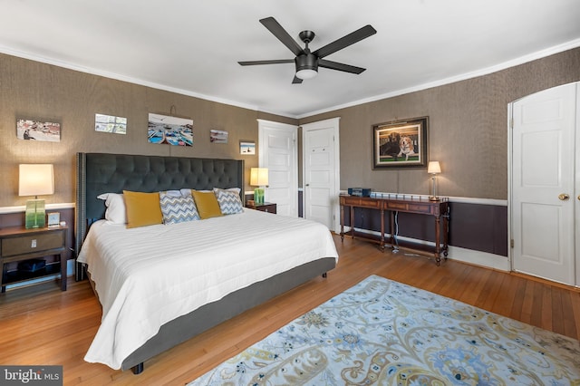 bedroom with wallpapered walls, a ceiling fan, wood finished floors, and ornamental molding