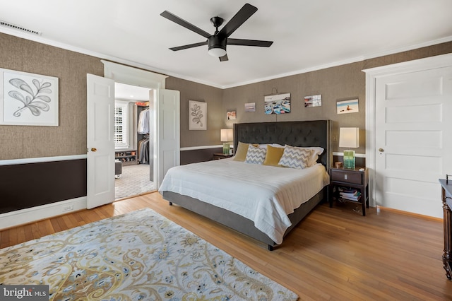 bedroom with visible vents, hardwood / wood-style floors, crown molding, wallpapered walls, and baseboards