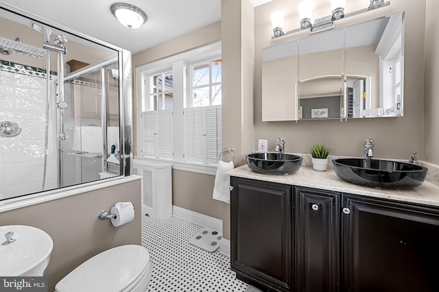 bathroom featuring a shower stall, toilet, double vanity, and a sink