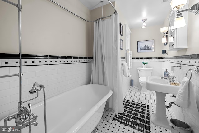 full bath with tile patterned flooring, a wainscoted wall, toilet, a freestanding tub, and tile walls