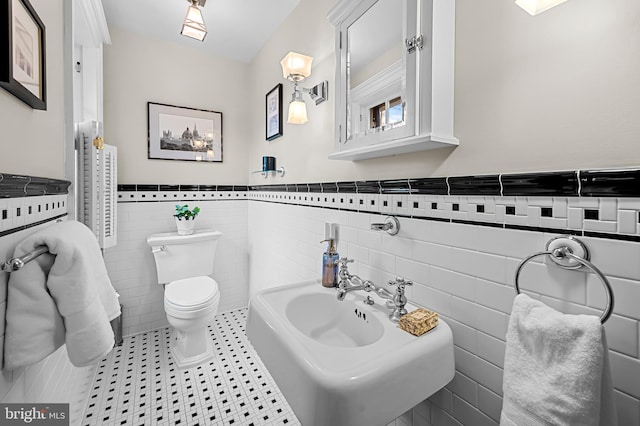 bathroom with tile patterned floors, toilet, a sink, tile walls, and wainscoting