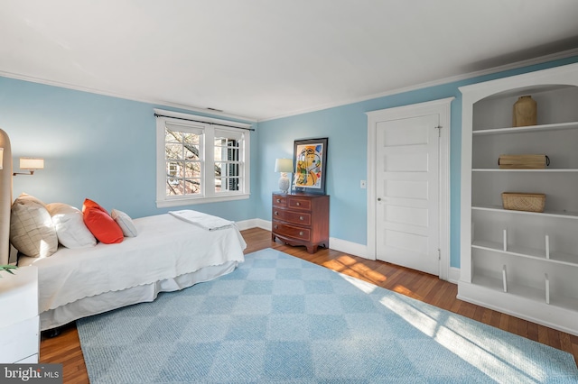 bedroom with wood finished floors, baseboards, and ornamental molding