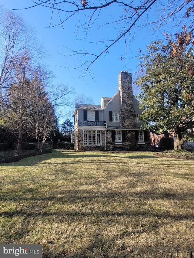 rear view of house featuring stone siding, a chimney, and a yard