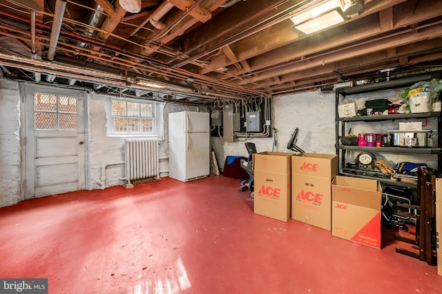 below grade area featuring electric panel, radiator heating unit, and freestanding refrigerator