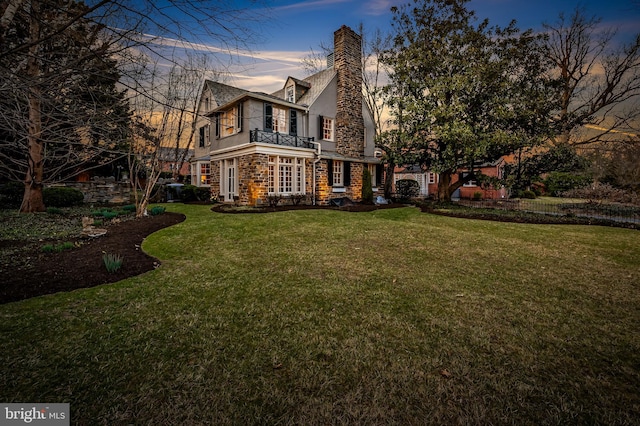 view of front of home featuring stucco siding, stone siding, a yard, and a chimney